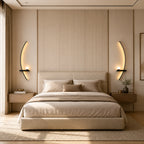 Pair of black crescent arc LED bedside wall lights flanking a bed, curved inward in a modern hotel-style bedroom.