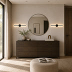 Black rechargeable wireless minimalist wall lights either side of a round mirror above a bedroom dresser
