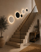 Black halo LED wall lights on a staircase wall, triggering automatically with motion sensor as someone walks past.