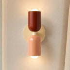 Colourful Nordic indoor wall light — red and pink cylindrical shades on a cream backplate for a warm romantic feel.