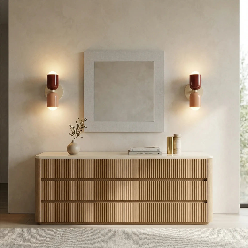 Pair of colourful Nordic metal wall lights with red and pink cylindrical shades mounted either side of a mirror above a wooden dresser