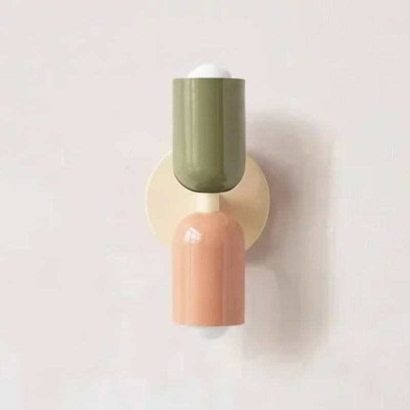 Colourful Nordic metal wall light with two cylindrical shades in green and pink on a cream base, casting light up and down