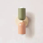 Colourful Nordic metal wall light with two cylindrical shades in green and pink on a cream base, casting light up and down