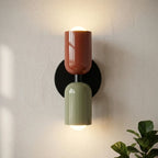 Colourful Nordic metal wall light with two cylindrical shades in red and green on a black base, casting a warm ambient glow up and down
