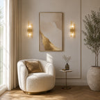 Gold column crystal glass Art Deco wall sconces flanking framed abstract artwork in elegant panelled living room with armchair