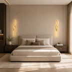 Pair of gold sculptural dual-curve LED wall lights either side of a bed in a luxury neutral bedroom