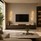Gold sculptural dual-curve LED wall lights flanking a wall-mounted TV in a warm modern living room with bookshelf