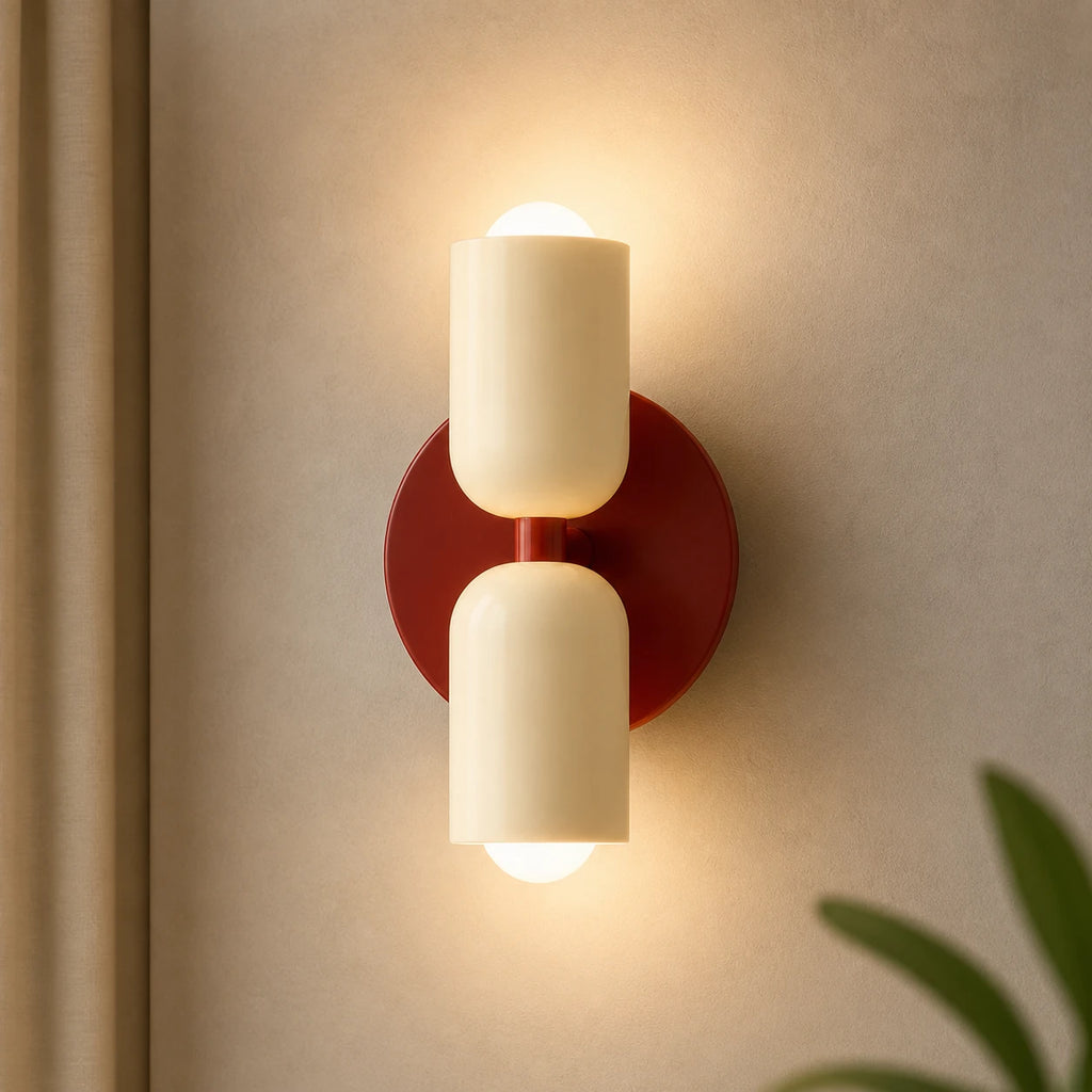 Two-tone Nordic indoor LED wall light with cream cylindrical shades glowing warmly in both directions against a neutral wall.