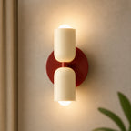 Two-tone Nordic indoor LED wall light with cream cylindrical shades glowing warmly in both directions against a neutral wall.