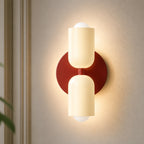 Two-tone Nordic indoor LED wall light with cream cylindrical shades on a red backplate casting warm ambient glow up and down.